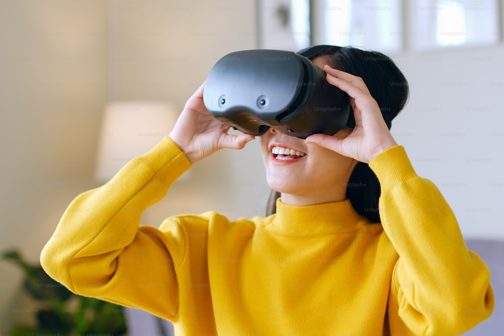 Joven asiática que se siente emocionada mientras usa auriculares 360 VR para realidad virtual / metaverso en casa