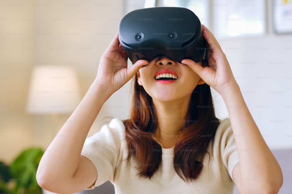 Joven asiática que se siente emocionada mientras usa auriculares 360 VR para realidad virtual / metaverso en casa