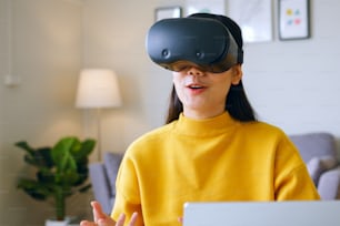 Jeune femme asiatique parlant tout en utilisant un casque VR 360 pour une réunion en ligne dans le métavers à la maison