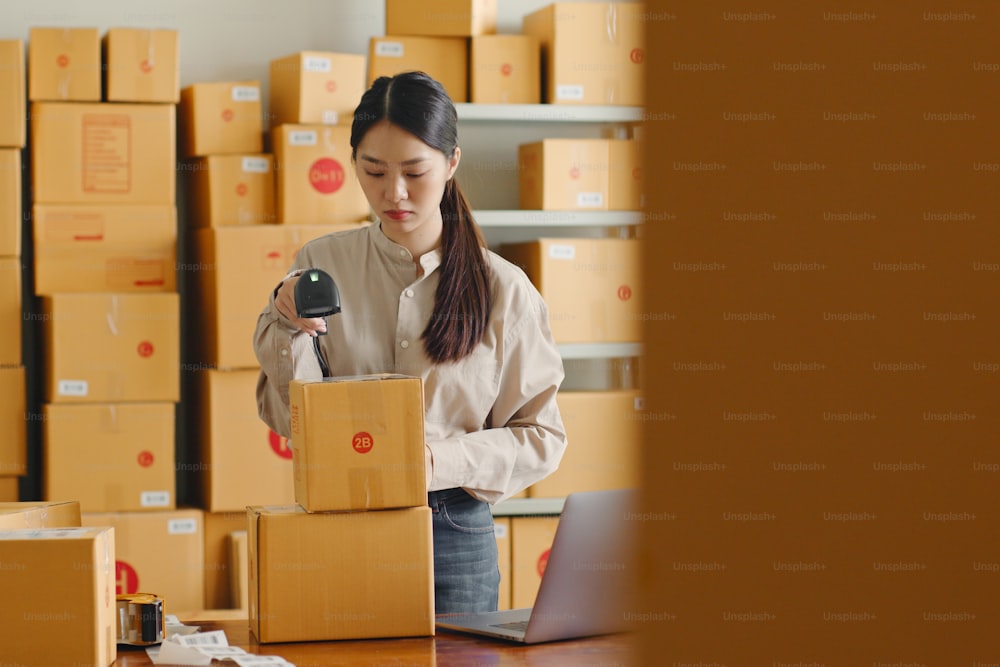 Asiatische Frau, die im Online-Shop-Lager arbeitet, mit Barcode-Leser, Überprüfung des Kundenpaketkastens, Online-E-Commerce-Einzelhandelskonzept für kleine Unternehmen