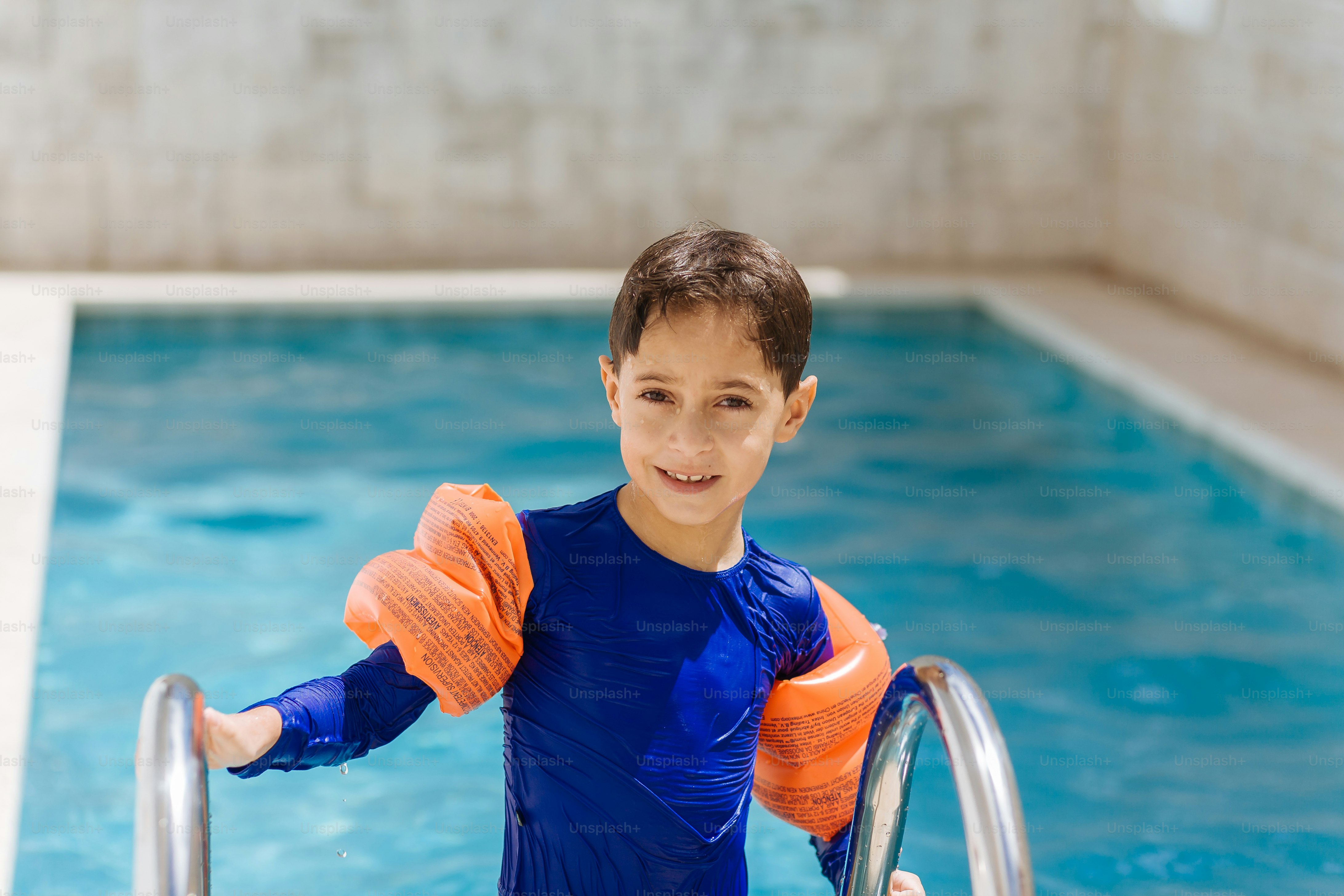 Süßer kleiner Junge im Badeanzug mit Armschwimmer im Pool
