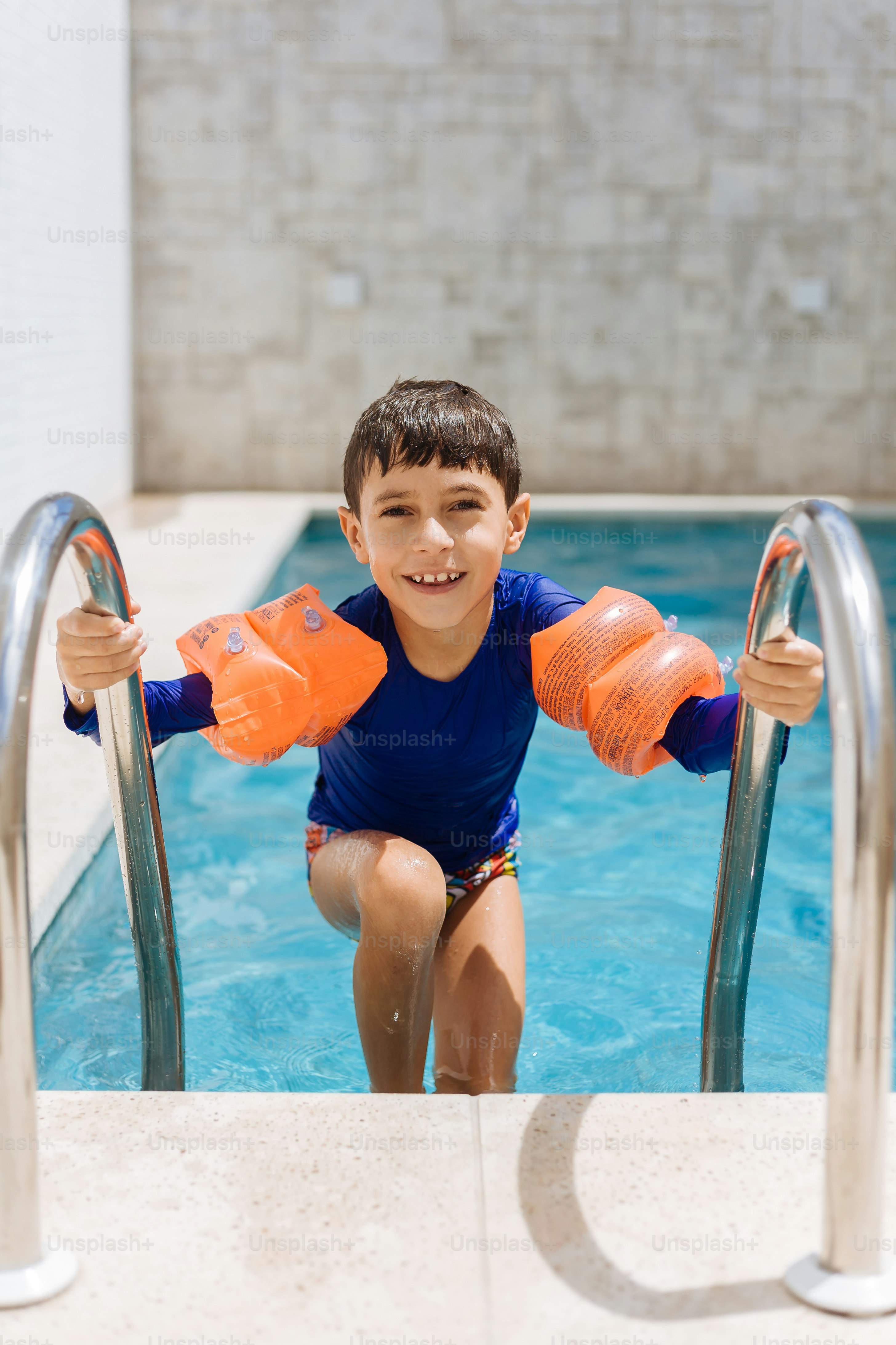 Süßer kleiner Junge im Badeanzug mit Armschwimmer im Pool