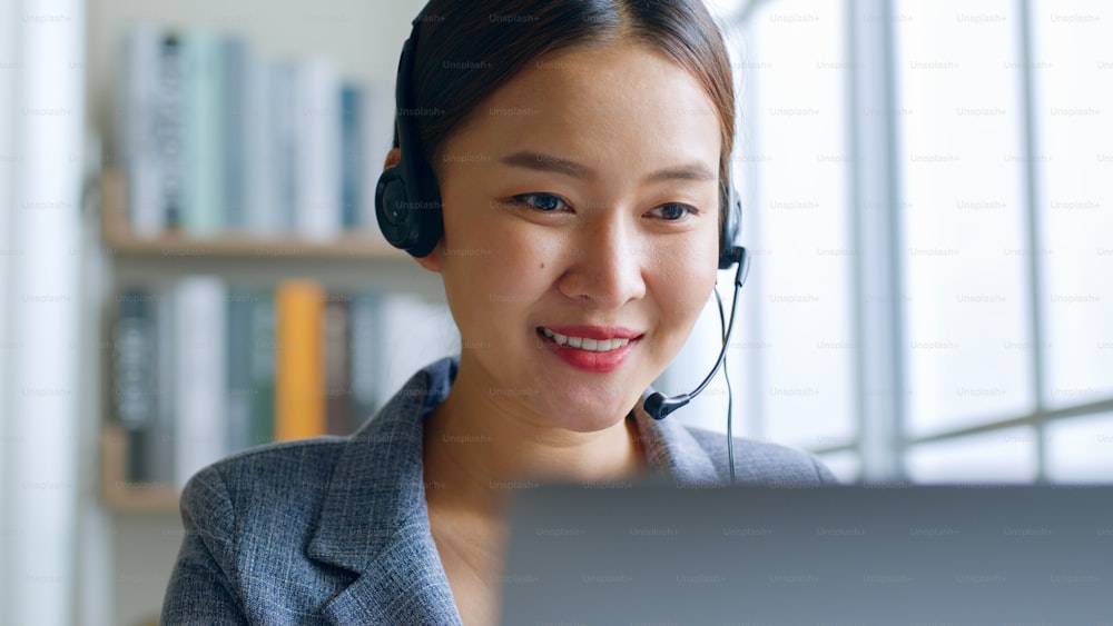 Gros plan d’une jeune femme d’affaires asiatique portant un casque, un centre d’appels, un service client parlant lors d’une vidéoconférence ou d’une réunion virtuelle au bureau