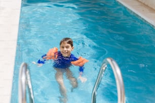 Dulce niño en traje de baño con flotador de brazo en la piscina