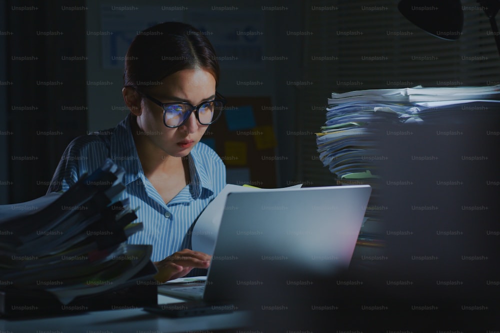 Dipendente d'ufficio asiatico sovraccarico di lavoro che utilizza un computer portatile per lavorare a tarda notte in ufficio. Lavoro straordinario di notte