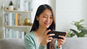 Lächeln junge asiatische Frau, die Smartphone benutzt, um Spiele zu spielen und in sozialen Medien zu Hause zu chatten.