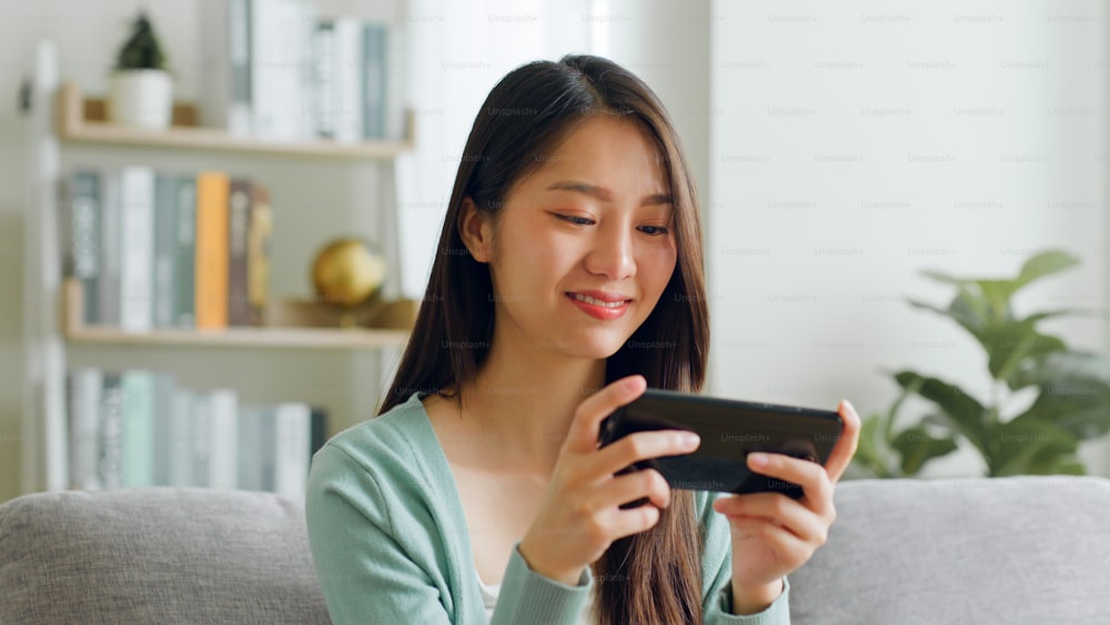 Smile young Asian woman using smartphone to play game and chatting in social media at home.