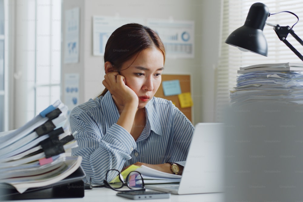 Versuchte asiatische Büroangestellte, die sich gelangweilt, unglücklich und ausgebrannt fühlt, im Büro zu arbeiten