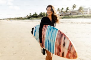 Retrato da mulher jovem do surfista na praia segurando sua prancha de surf