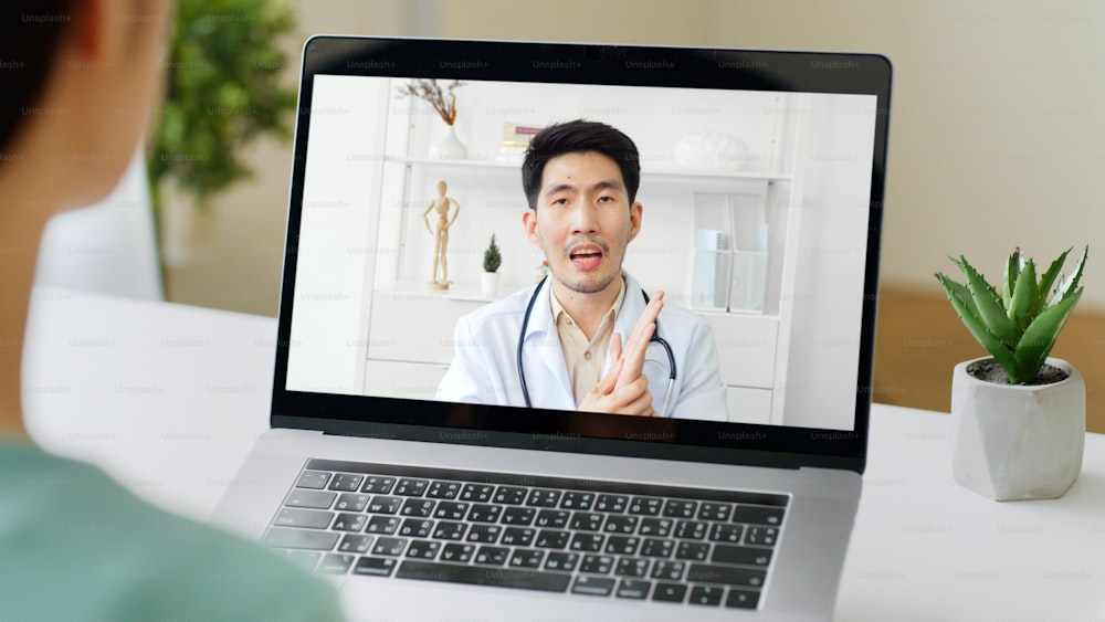 Asian woman talking with doctor via computer laptop virtual video call or video conference at home, telehealth and telemedicine concept