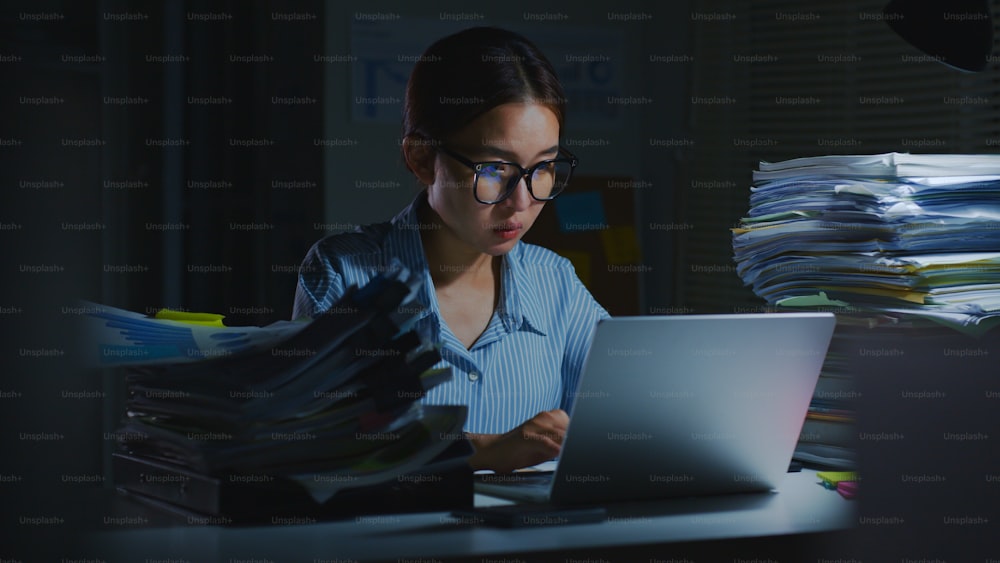 Dipendente d'ufficio asiatico sovraccarico di lavoro che utilizza un computer portatile per lavorare a tarda notte in ufficio. Lavoro straordinario di notte