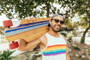 Bel homme avec planche à roulettes portant un t-shirt aux couleurs de l’arc-en-ciel comme symbole de la fierté LGBT