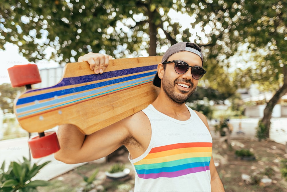 Homem bonito com skate vestindo camiseta colorida arco-íris como símbolo do orgulho LGBT
