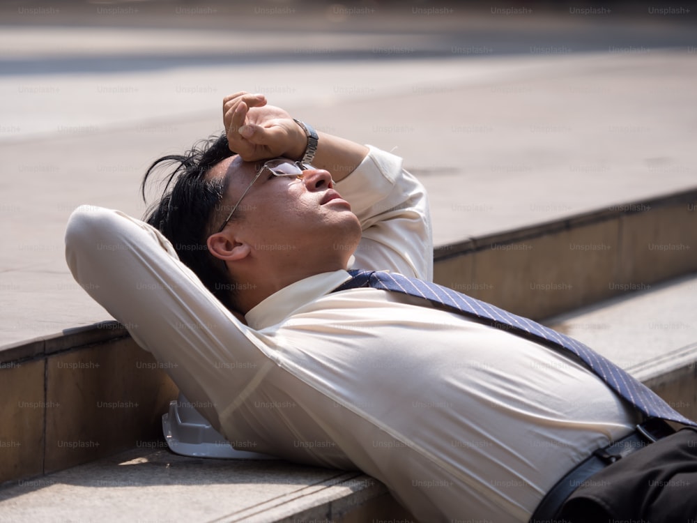 Verärgerter asiatischer Geschäftsmann 40er Jahre müde von der Arbeit sitzen an der Treppe, Arbeitslosigkeit, vom Job entlassen, enttäuscht, Verlust und Gefühl der Niedergeschlagenheit Konzept