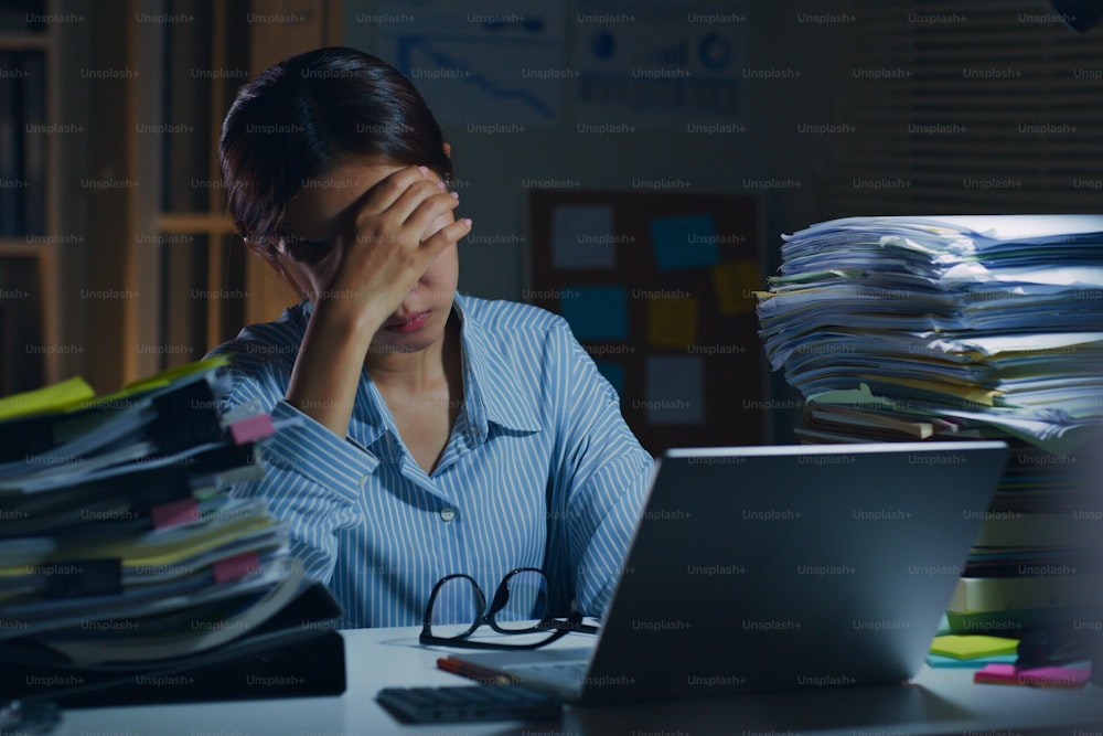 Giovane impiegato d'ufficio asiatico che si sente stanco, affaticamento, esausto mentre fa gli straordinari di notte in ufficio