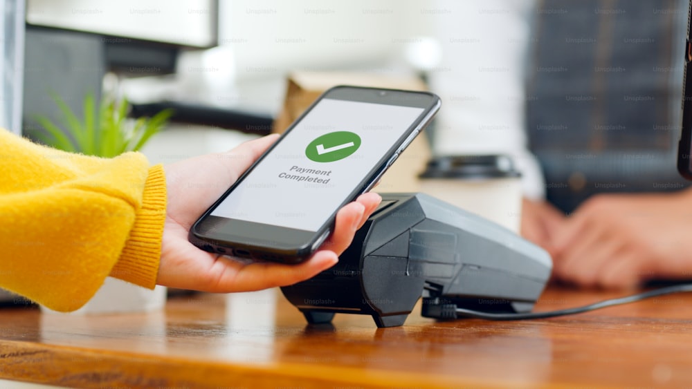 El cliente usa un teléfono inteligente para el pago NFC en el restaurante cafetería, tecnología sin efectivo, sin contacto y concepto de transferencia de dinero