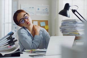 Impiegato d'ufficio asiatico stanco che massaggia i muscoli del collo e delle spalle affaticato dall'uso del computer portatile per lungo tempo, concetto di sindrome dell'ufficio