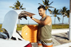 Young surfer taking his bodyboard out of the car trunk. Sport and water sport concept.