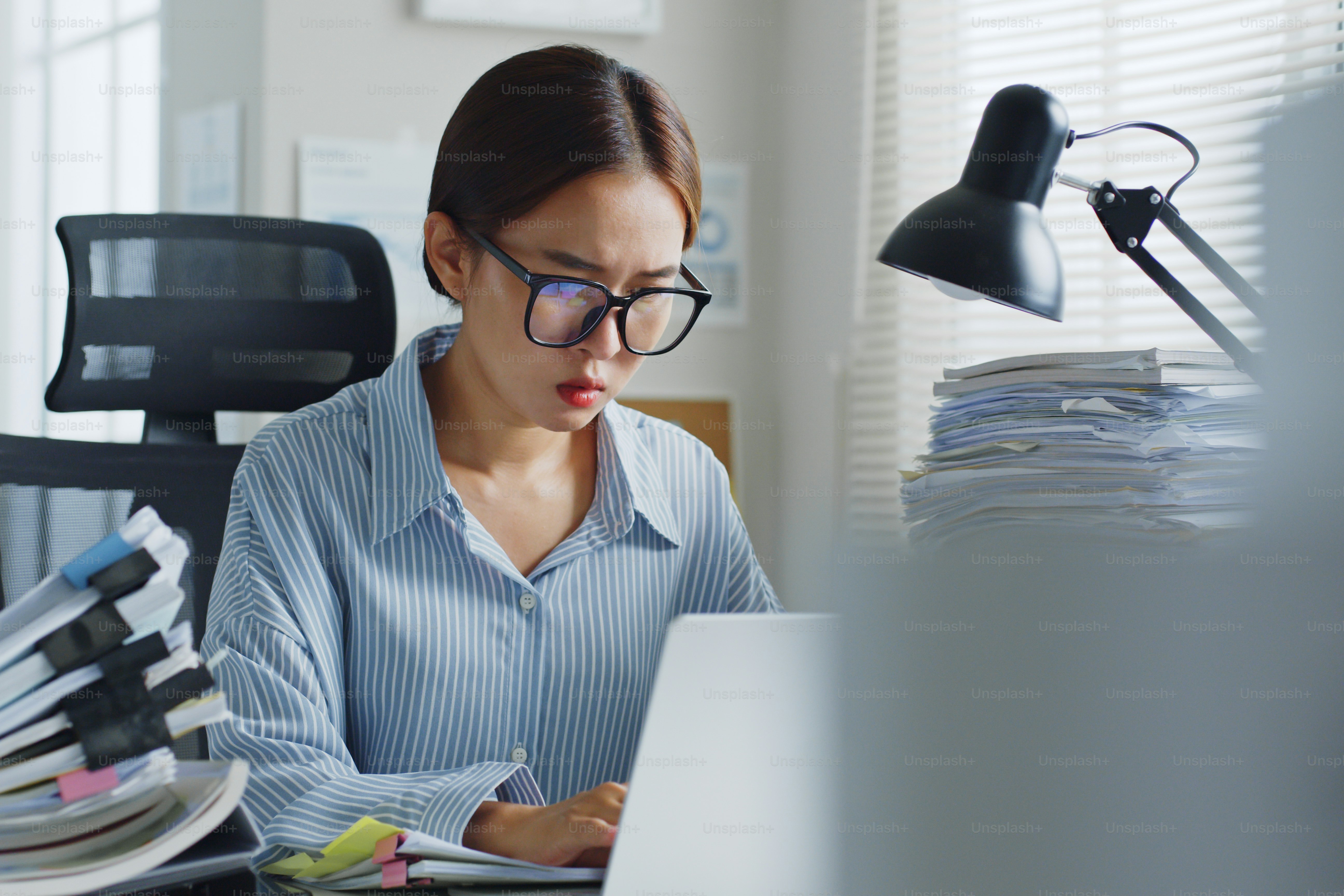 Asian woman office employee working on laptop computer, feeling serious stress and busy at office