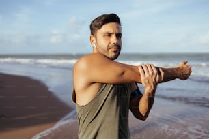 Athletic man stretching arms before exercise at the beach. Sport and healthy lifestyle.