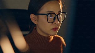 Young Asian woman, developer programmer, software engineer, IT support, wearing glasses working hard at night overtime on computer to check coding in bugging system and running program successful.