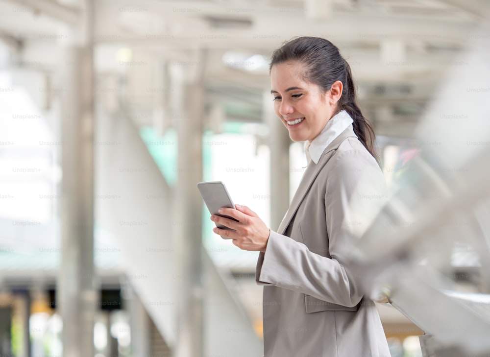 Portrait young caucasian businesswoman 20-30s holding smart phone/cell phone/mobile in formal suit at the modern city