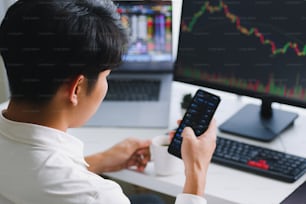 Jovem investidor asiático observando a mudança da criptomoeda e do mercado de ações no smartphone.