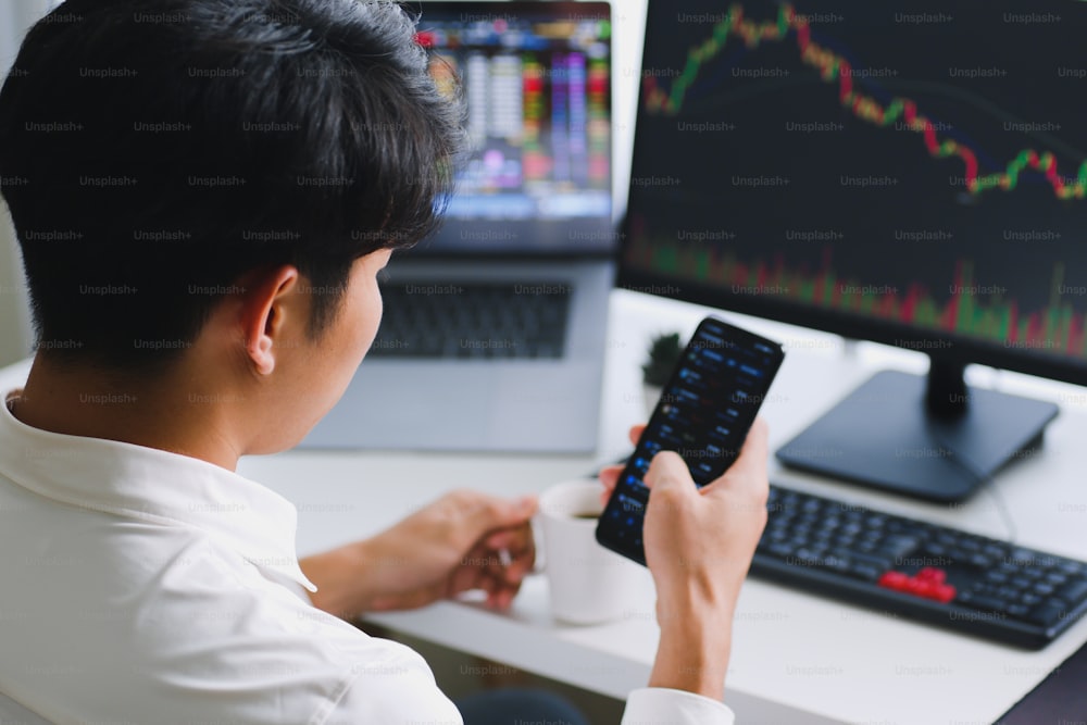 Giovane investitore asiatico che guarda il cambiamento della criptovaluta e del mercato azionario su smartphone.