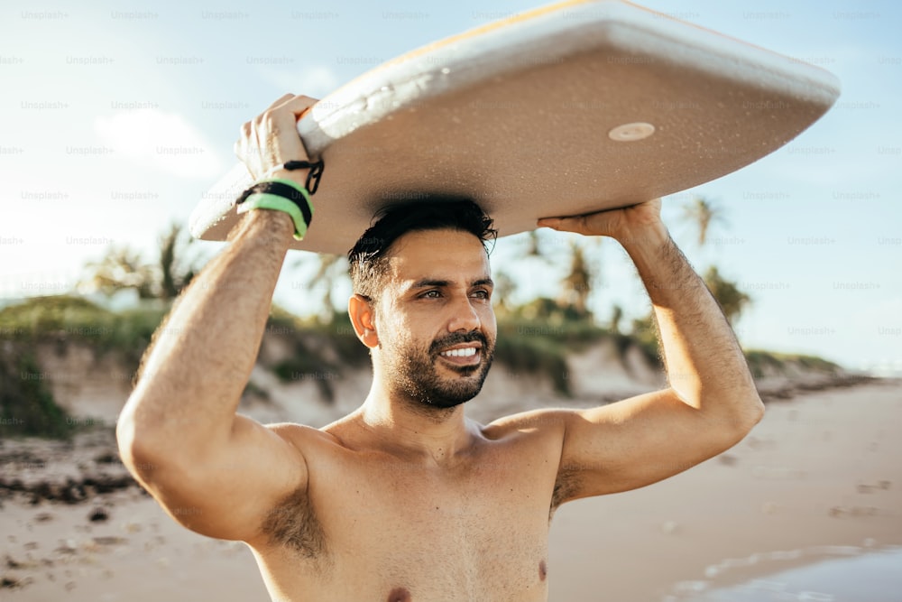 Porträt eines brasilianischen Surfers am Strand, der sein Bodyboard hochhält. Sport- und Wassersportkonzept.