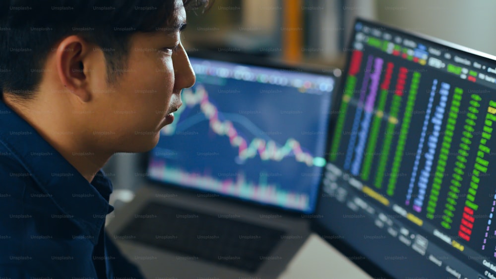 Junger asiatischer Investor, der die Veränderung des Aktienmarktes beobachtet und Aktien auf dem Computer-Laptop-Bildschirm handelt.