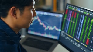 Joven inversor asiático que observa el cambio del mercado de valores y negocia acciones en la pantalla de la computadora portátil.