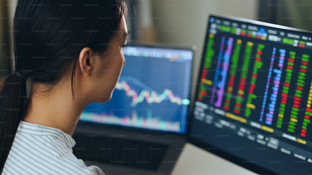 Junge asiatische Investorin, die die Veränderung des Aktienmarktes und den Aktienhandel auf dem Computer-Laptop-Bildschirm beobachtet.