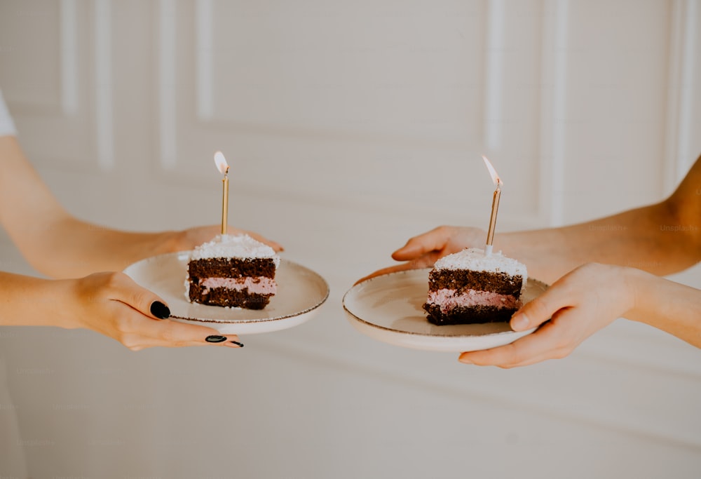two people holding plates with two slices of cake