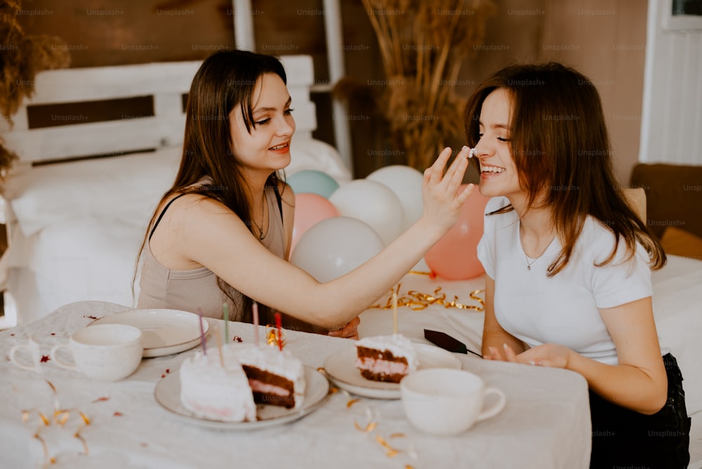 um casal de mulheres sentadas em uma mesa com bolo