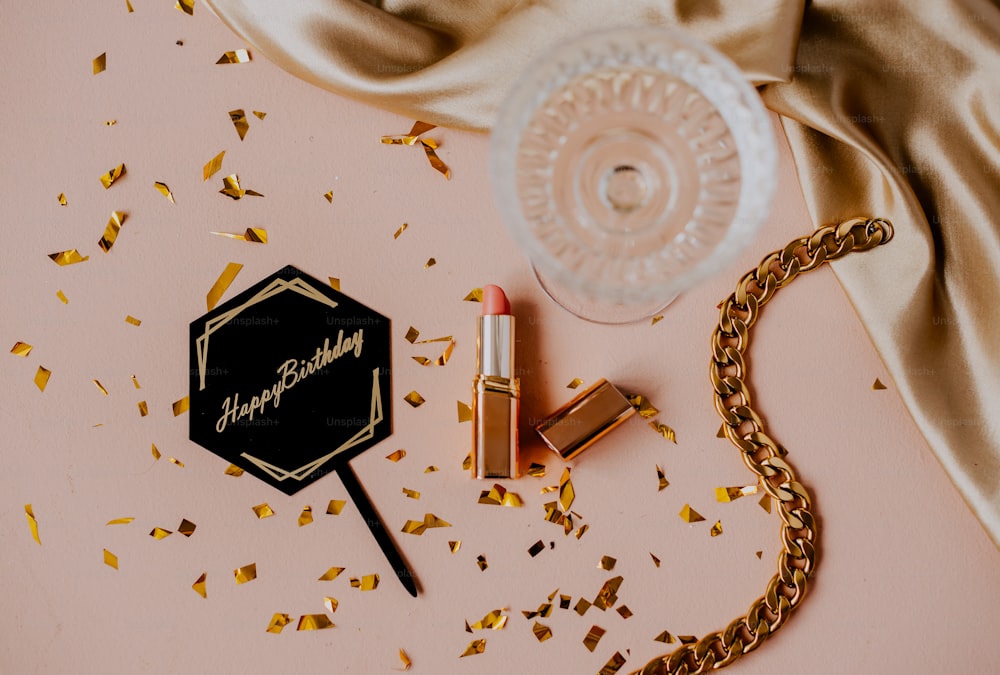 a gold necklace, lipstick, and a bottle of lipstick on a pink surface