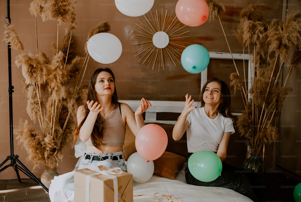 two women sitting on a bed with balloons