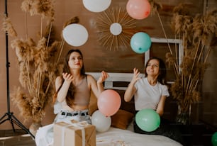 two women sitting on a bed with balloons