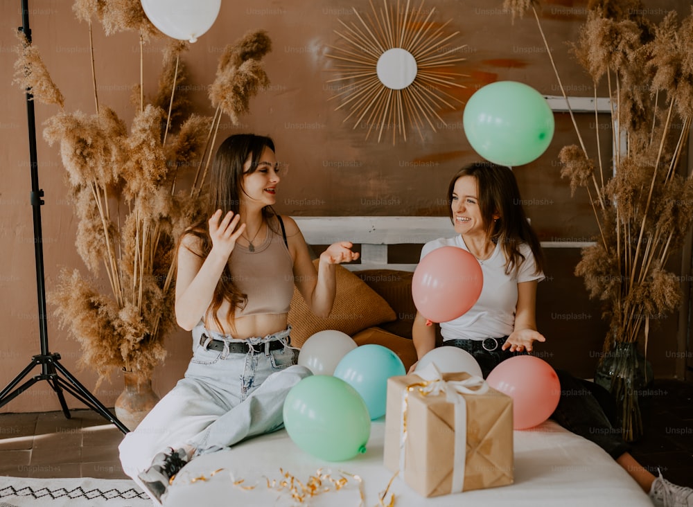duas mulheres sentadas em uma cama com balões