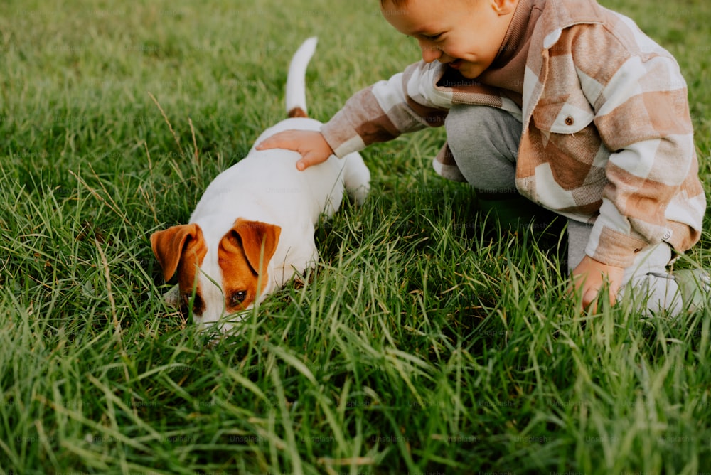 Ein kleiner Junge, der mit einem Hund im Gras spielt