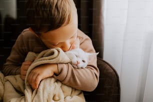 a young boy holding a white cat wrapped in a blanket