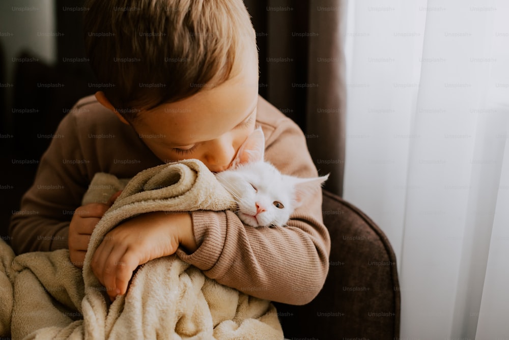 a young boy holding a white cat wrapped in a blanket