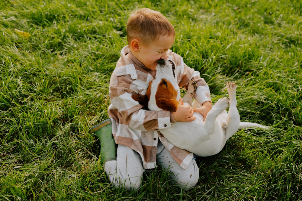 um menino sentado na grama com um cachorro