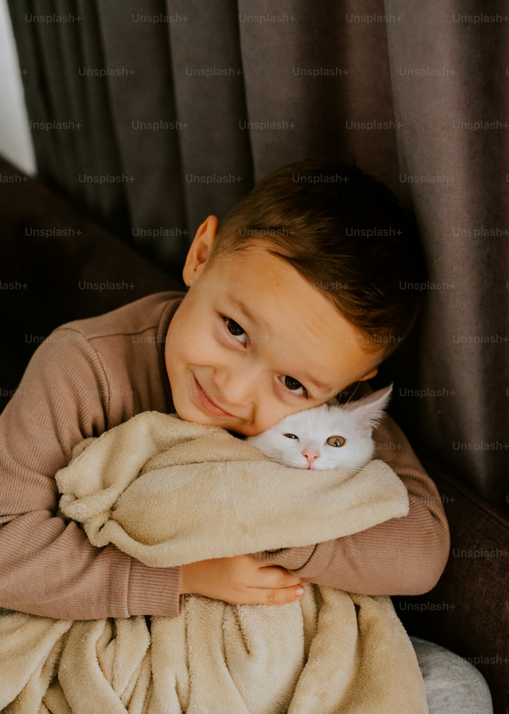 a young boy holding a cat wrapped in a blanket