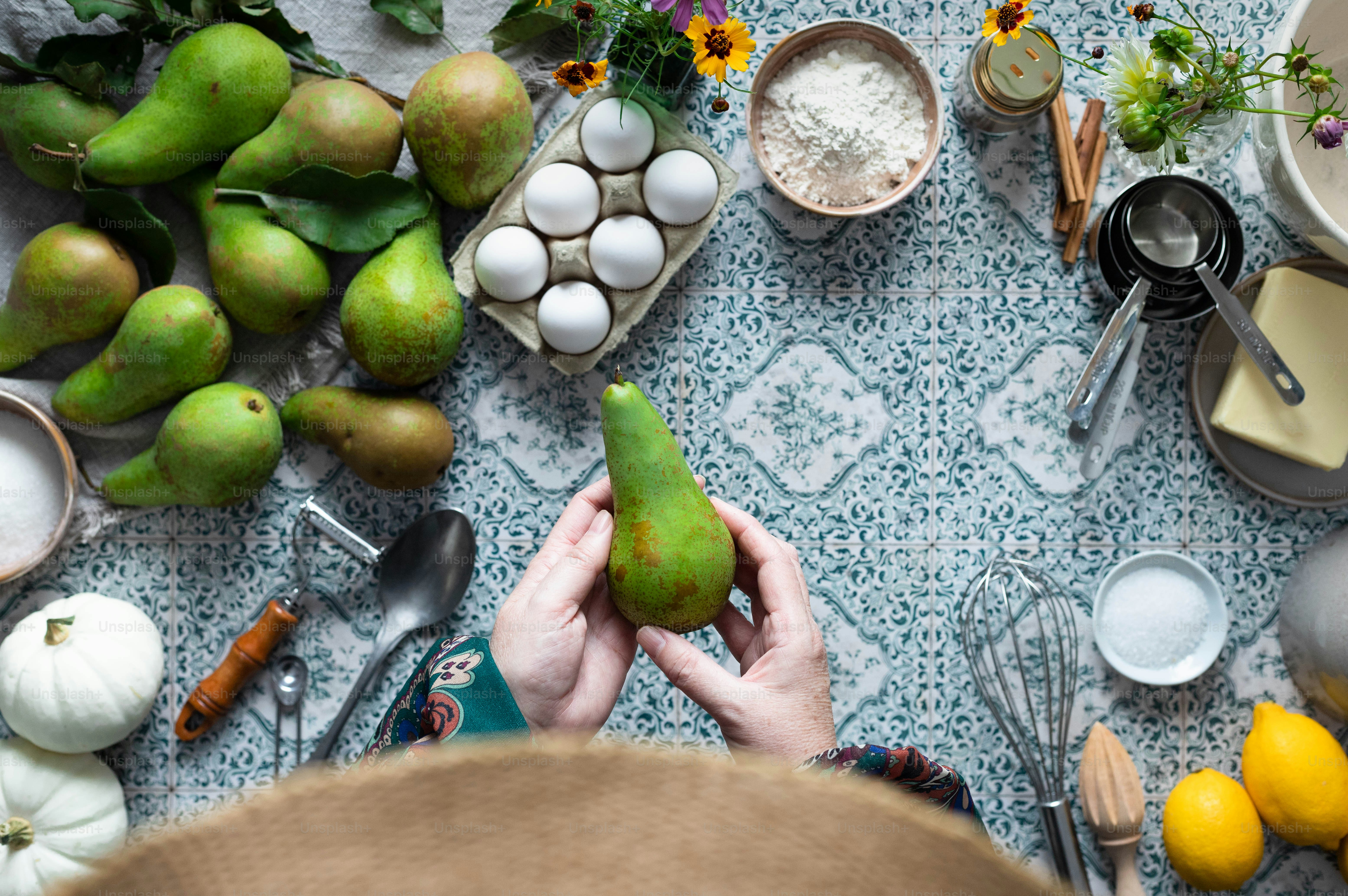 a person holding a pear in front of a table full of food