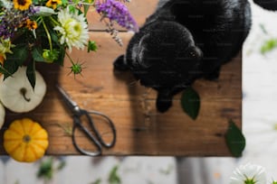 a black cat sitting on top of a wooden table next to a bunch of flowers