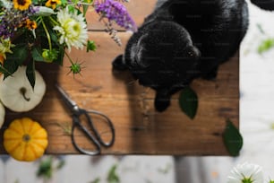 Eine schwarze Katze, die auf einem Holztisch neben einem Blumenstrauß sitzt