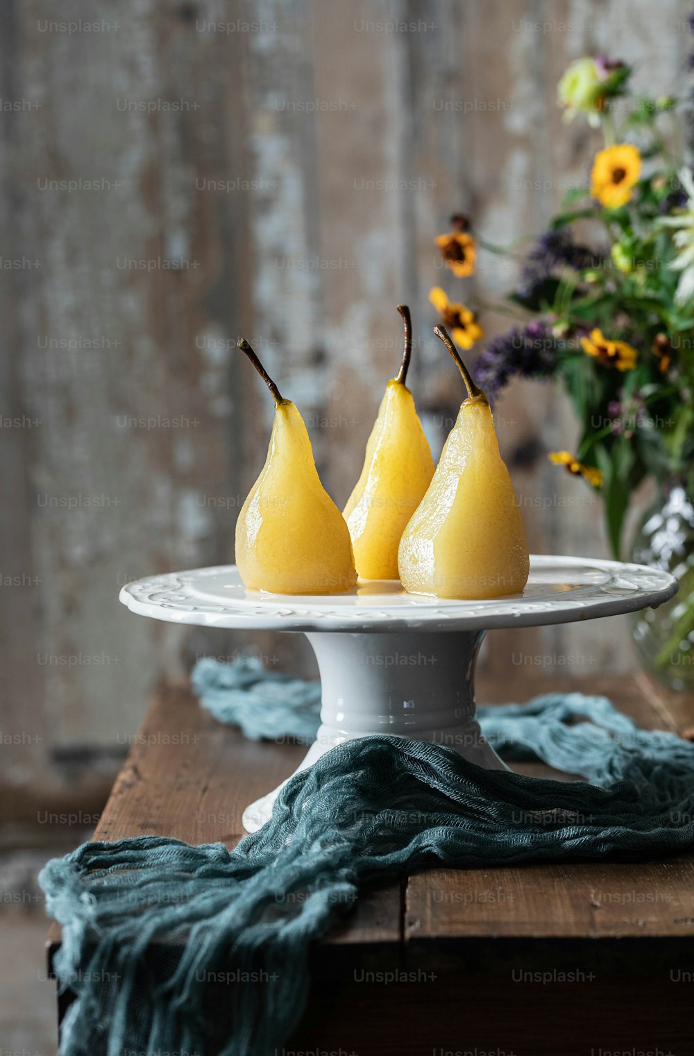 three pears on a white plate with flowers in the background