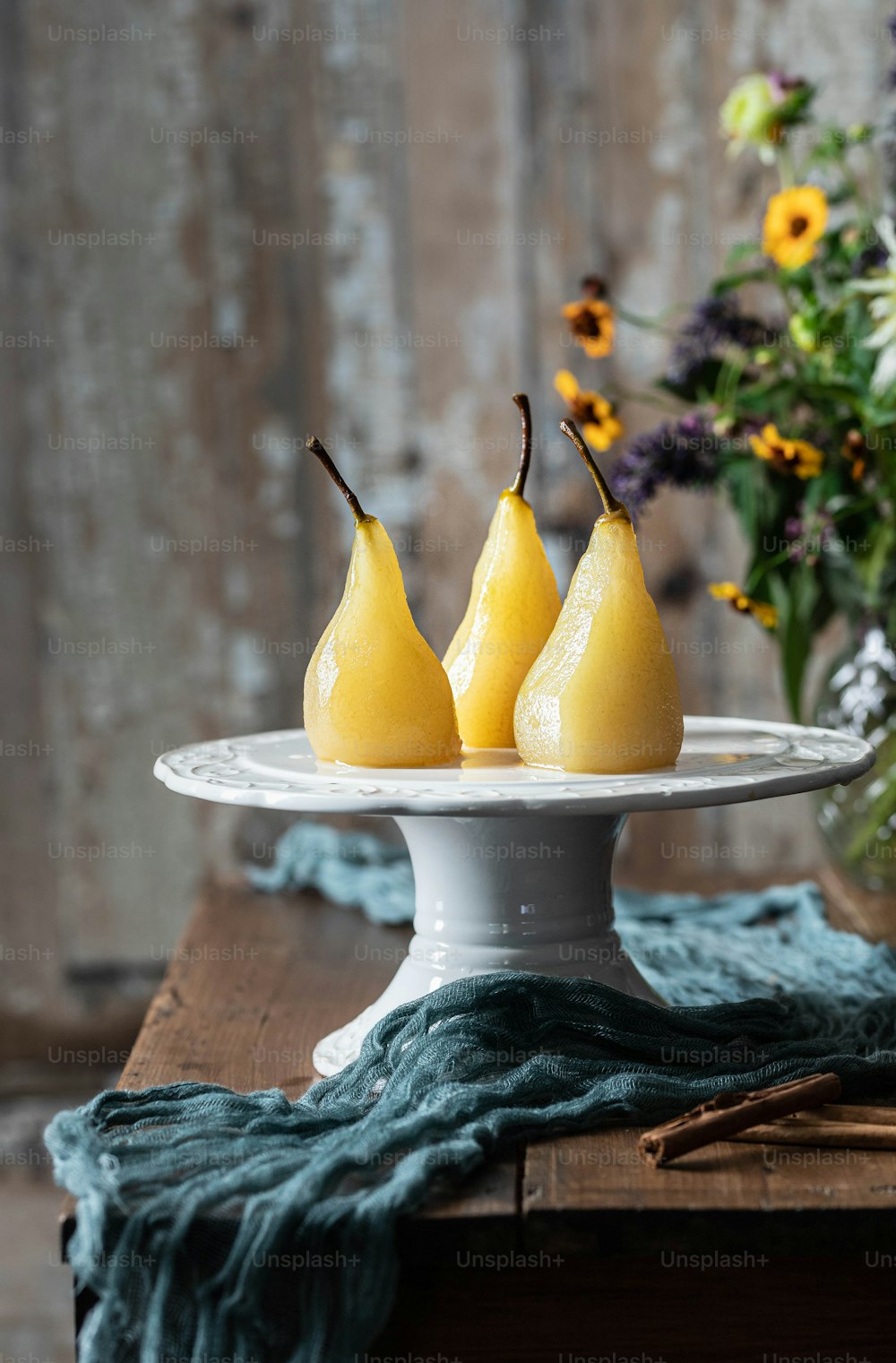 three pears on a white plate next to a vase of flowers