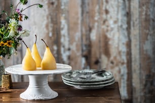 three pears on a cake plate next to a vase of flowers