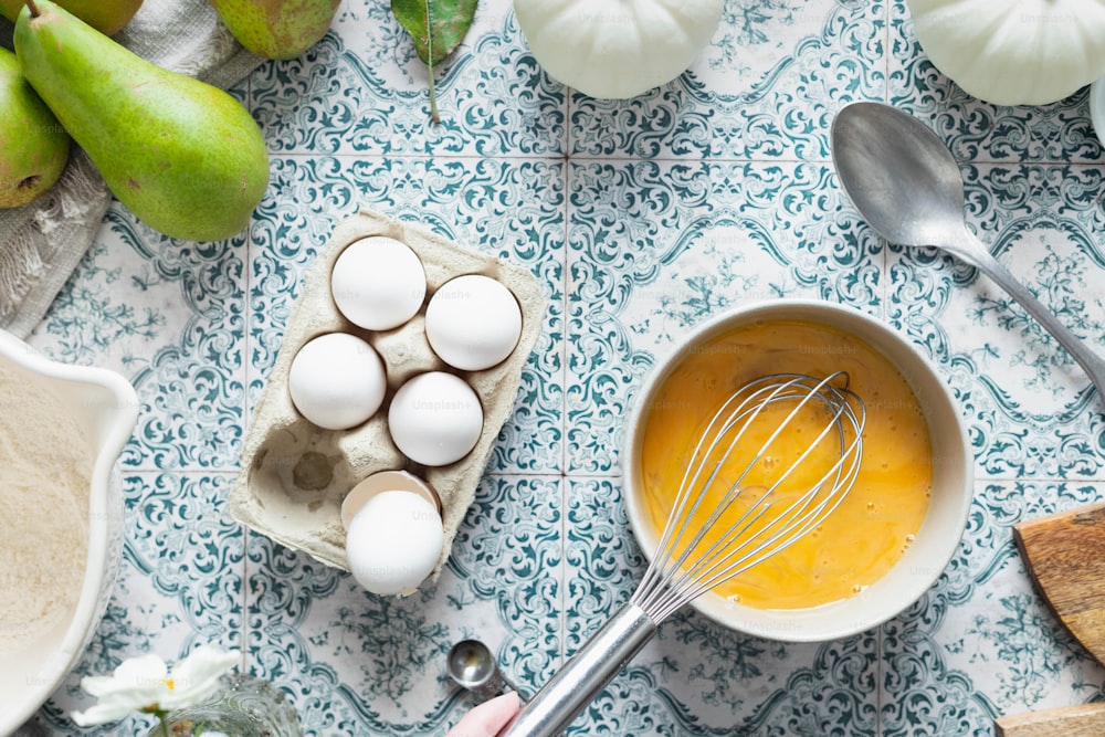 a bowl of eggs and a whisk on a table
